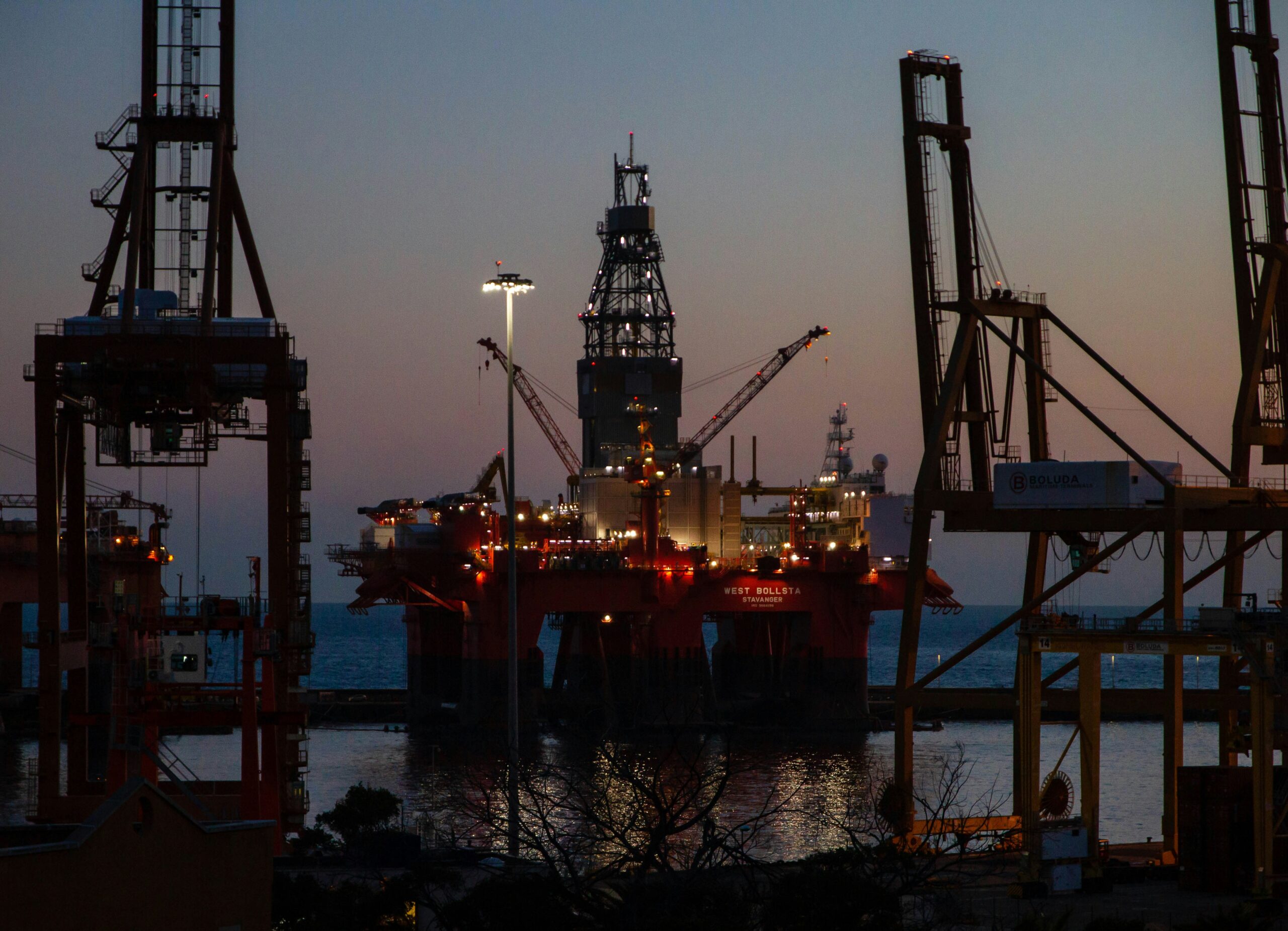 An offshore oil platform silhouetted at sunset, symbolizing global energy markets and their impact on USD oil correlation for prop traders.